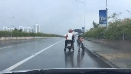 Clip cặp đôi đi xe máy đội mưa để che ô cho bé trai dắt xe đạp gây xúc động